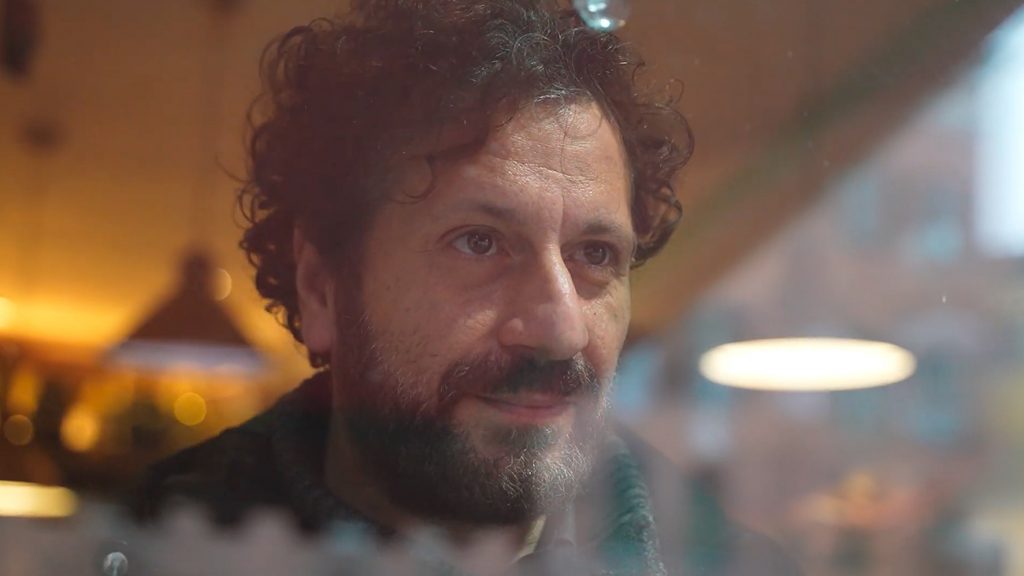 Primo piano di uomo barbuto osservato attraverso vetro con riflessi e luci calde